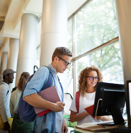 Two students interacting with a computer in a modern building.