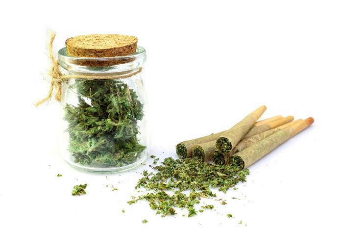 Glass jar with cannabis leaves, buds and rolled products